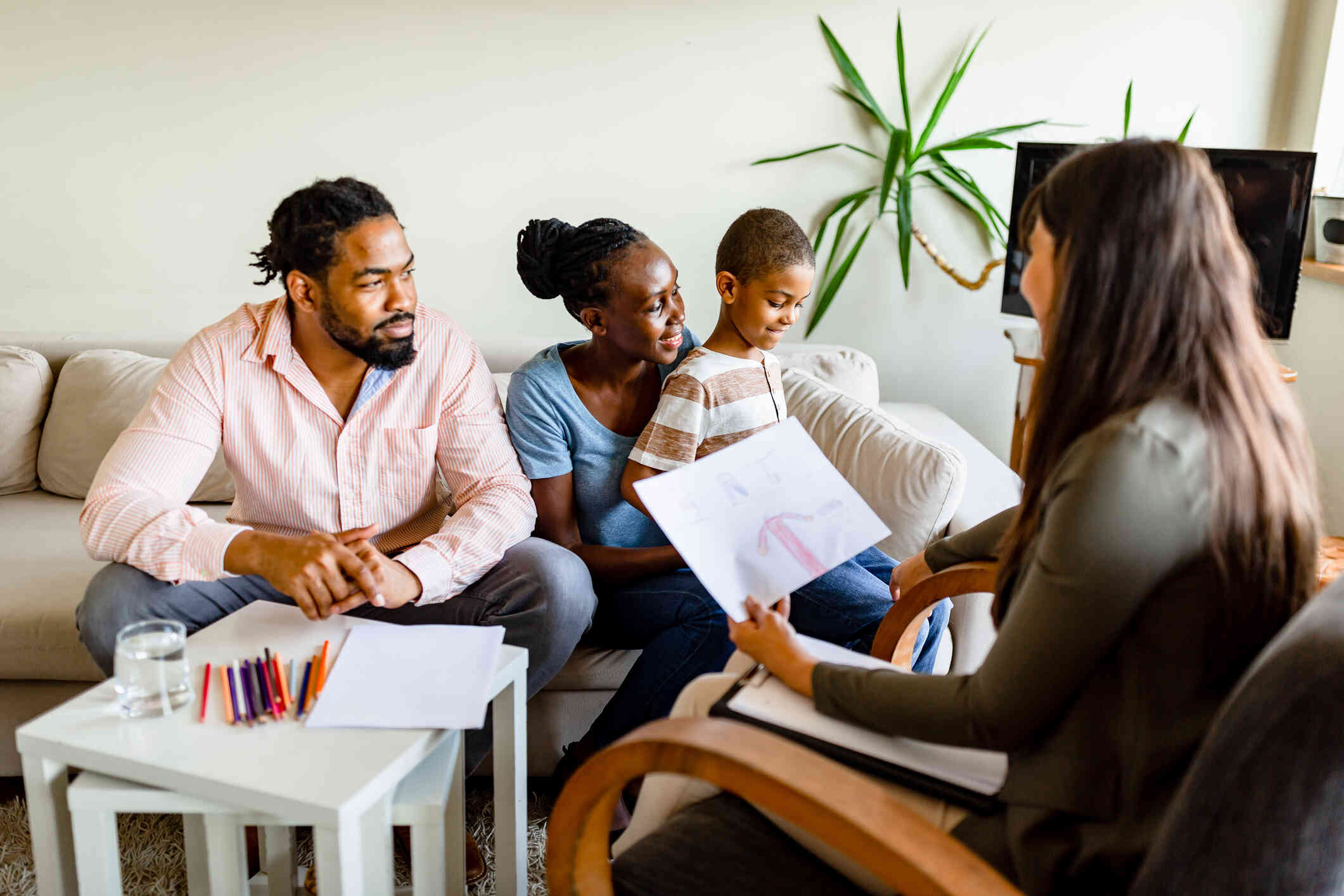 A family sits on a couch with their son with positive expressions while talking with a counselor holding a paper with a drawing